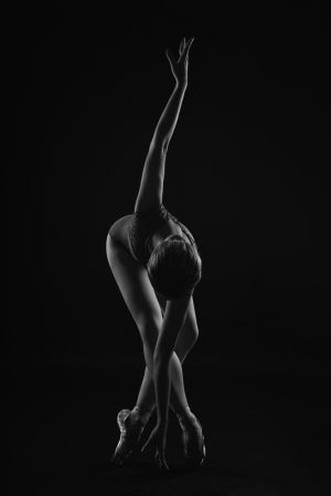 string. the ballerina is standing on pointe shoes leaning forward and wrapping her arm around